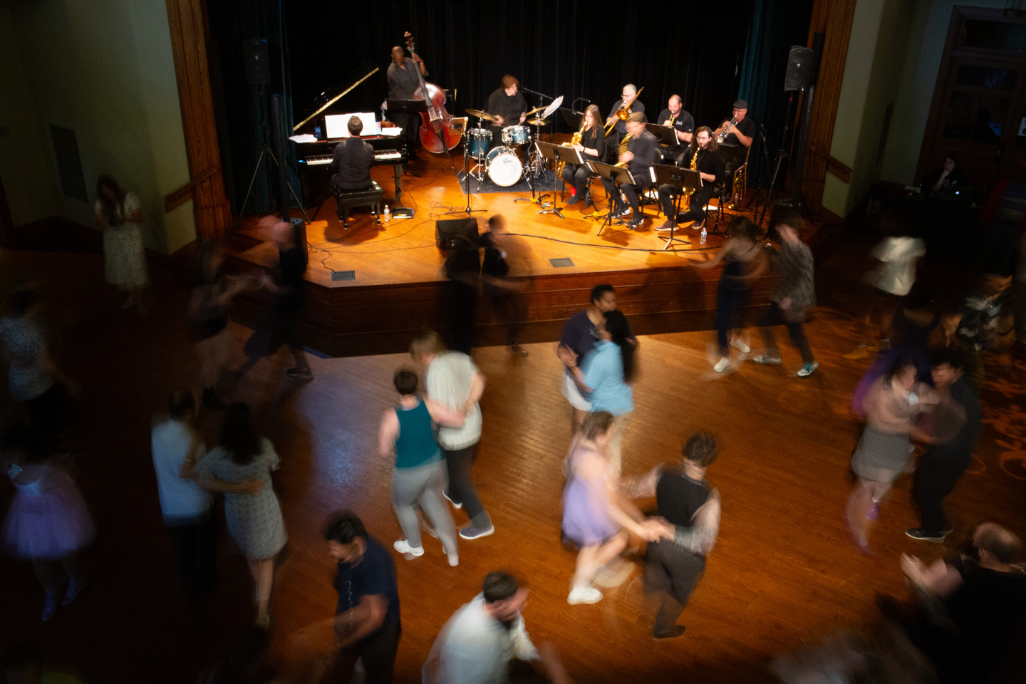 Overhead view of the full band on stage as couples swing dance across the floor below.