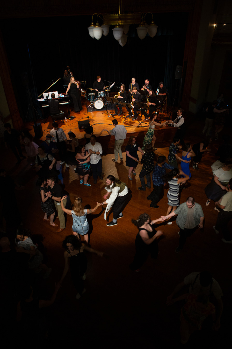 An overhead view of the band on stage with a crowd of couples swing dancing in the ballroom.