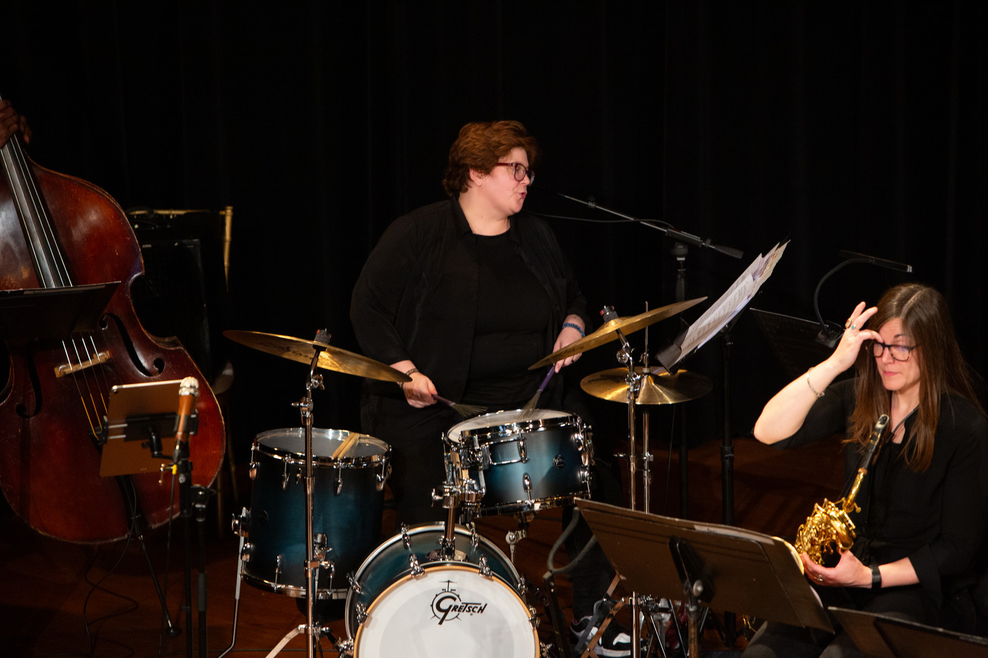 Chelsea Hughey playing the drum kit with a saxophonist and upright bassist alongside.