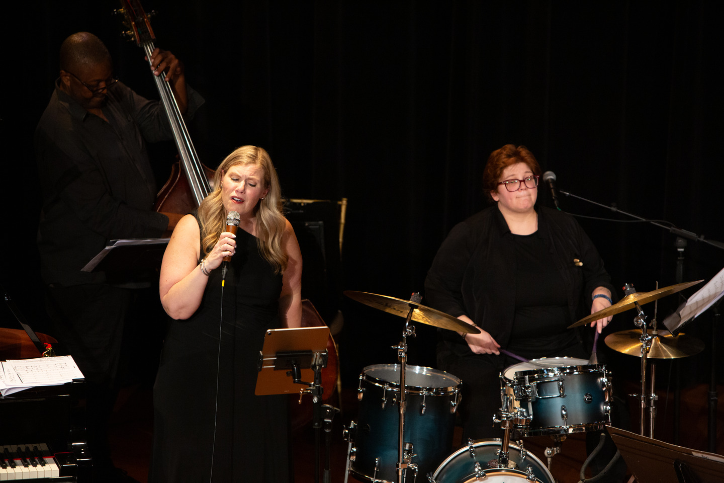 The vocalist singing beside the drummer, with the upright bassist behind them.