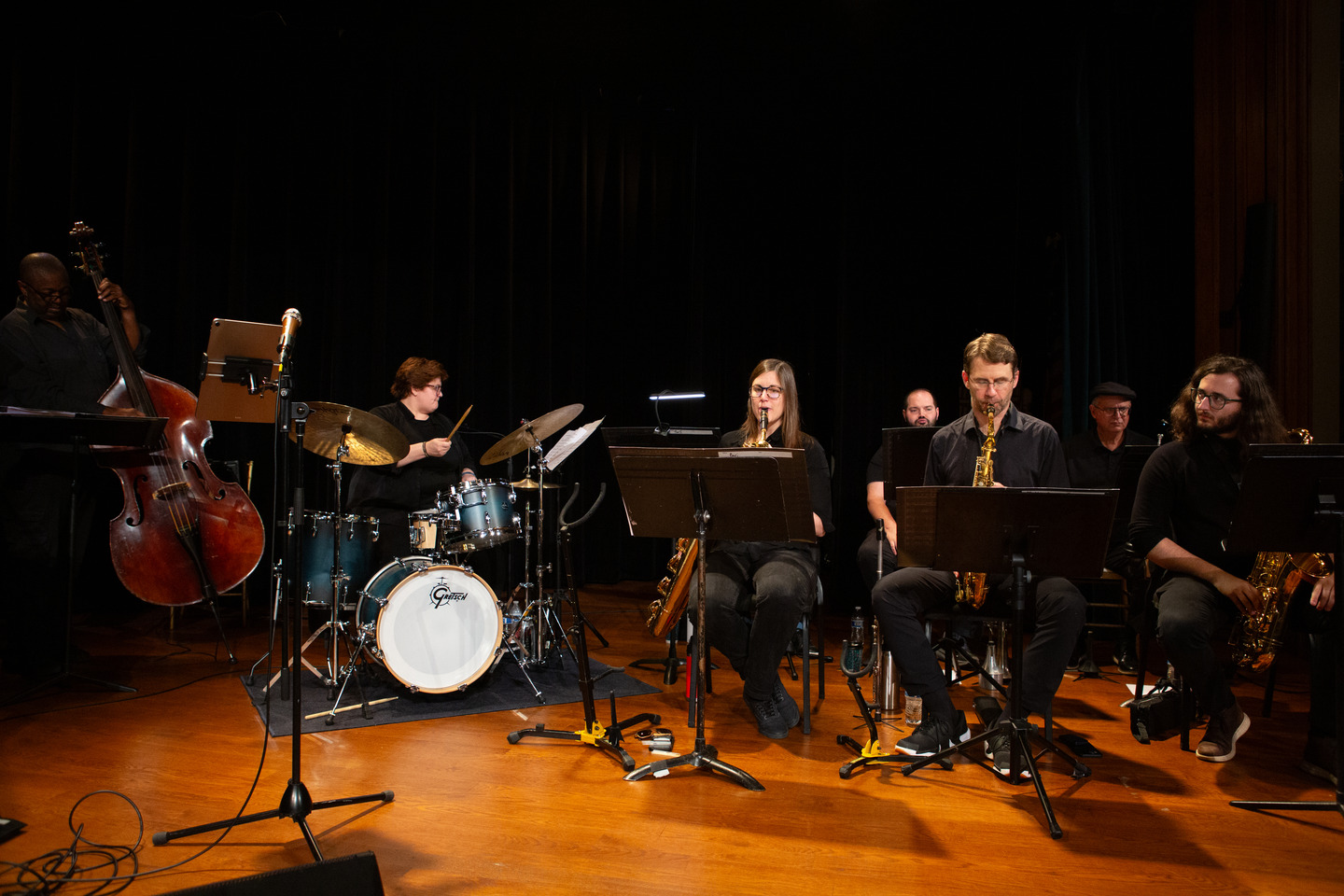 The full band seated across the stage — upright bass, drums, and the saxophone section performing.